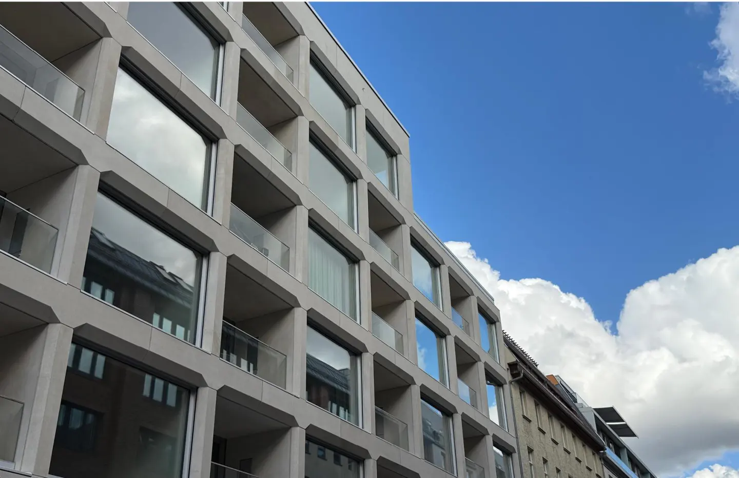 Modern apartment building with glass balconies against a blue sky with white clouds.