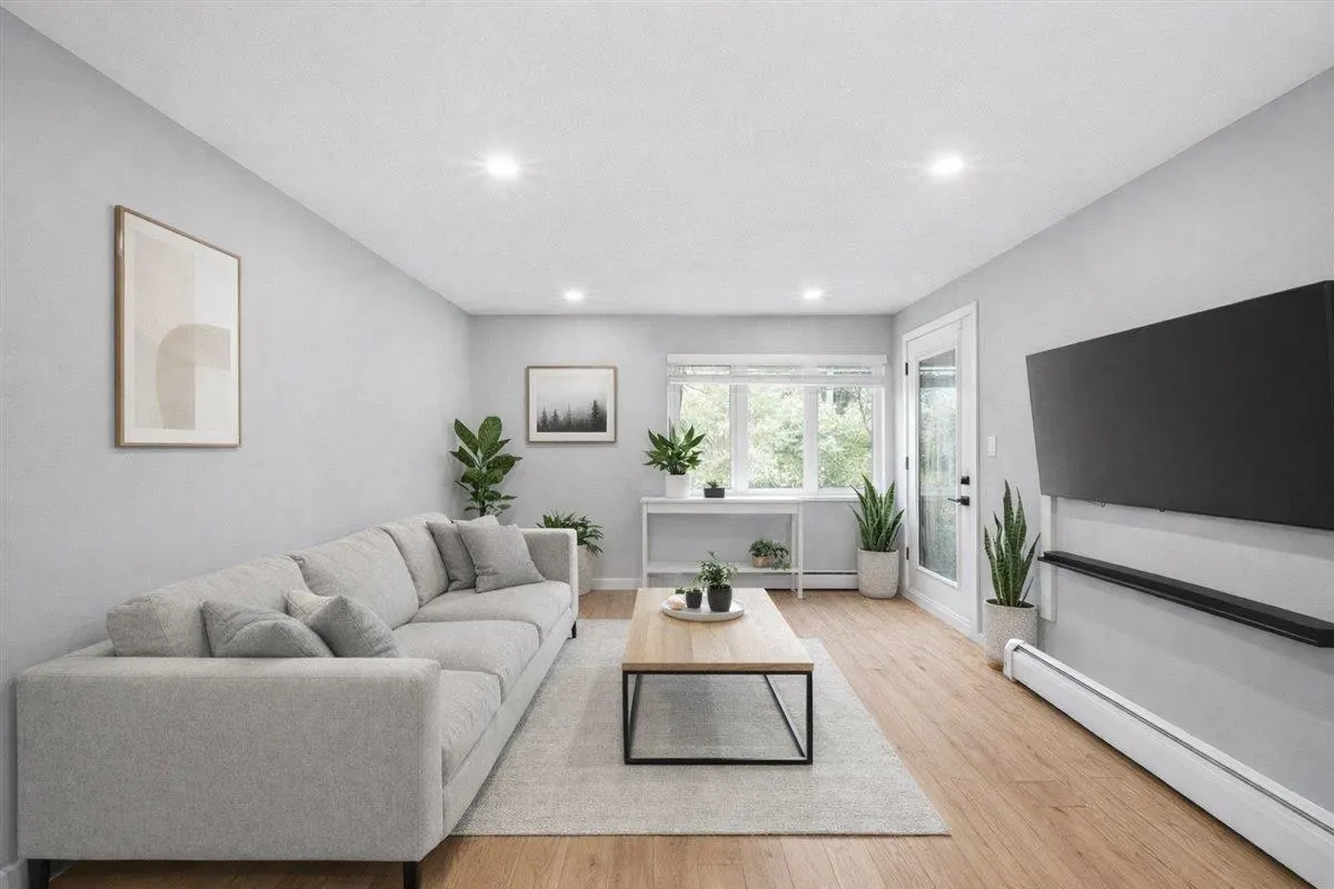 Bright living room with gray walls, wood floors, and a large gray sectional sofa. A black TV is mounted on the wall.