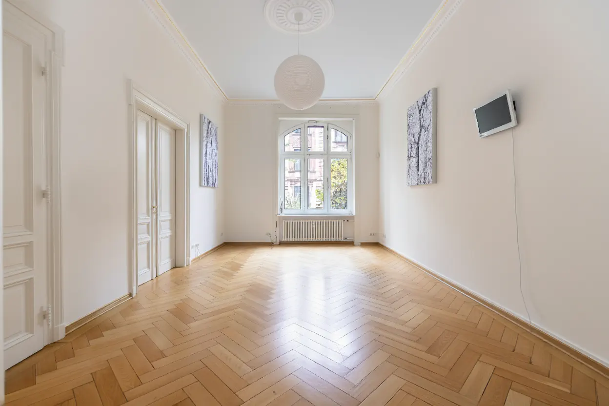Empty room with herringbone wood floor, white walls, large window, white doors, and modern art. A white globe light hangs from the ceiling.