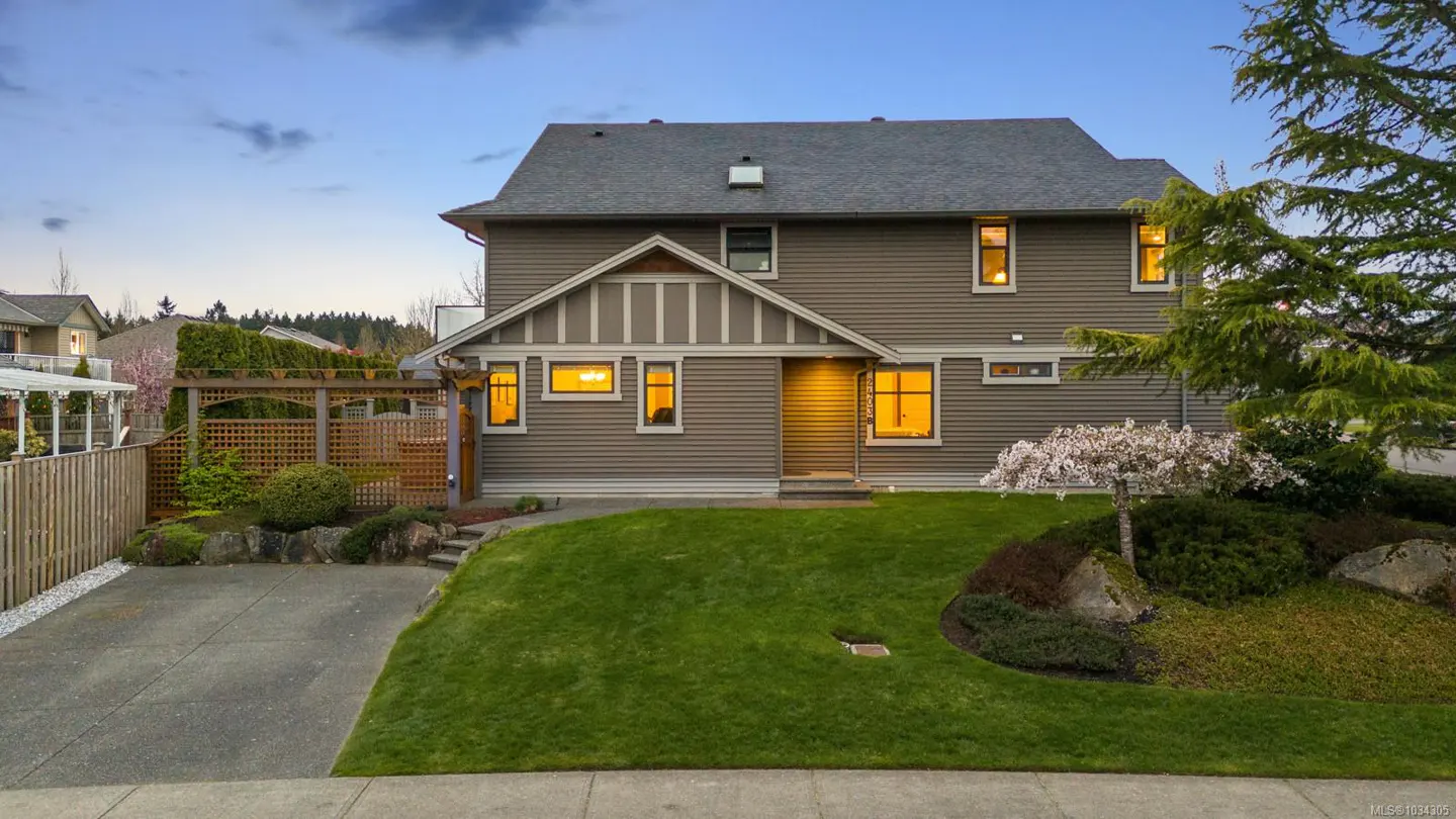 Two-story house with gray siding, a gray roof, and a green lawn at dusk. Lights are on inside.