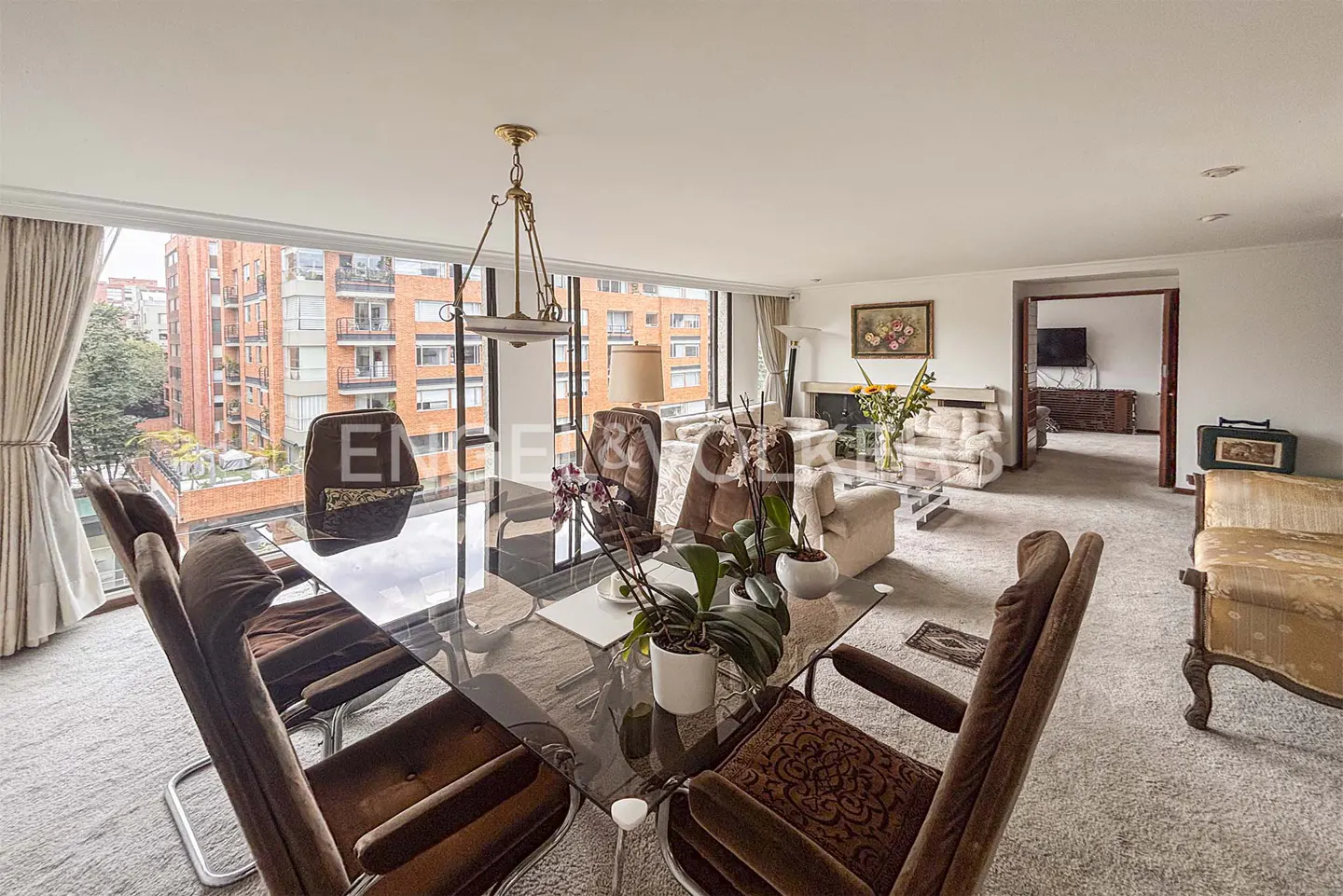 Open-concept living and dining area with a glass table, brown chairs, and a view of brick buildings.