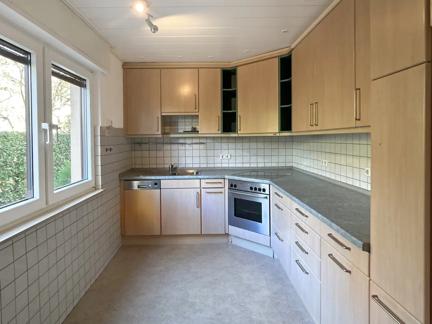 A bright kitchen with light wood cabinets, stainless steel appliances, and a window overlooking greenery.