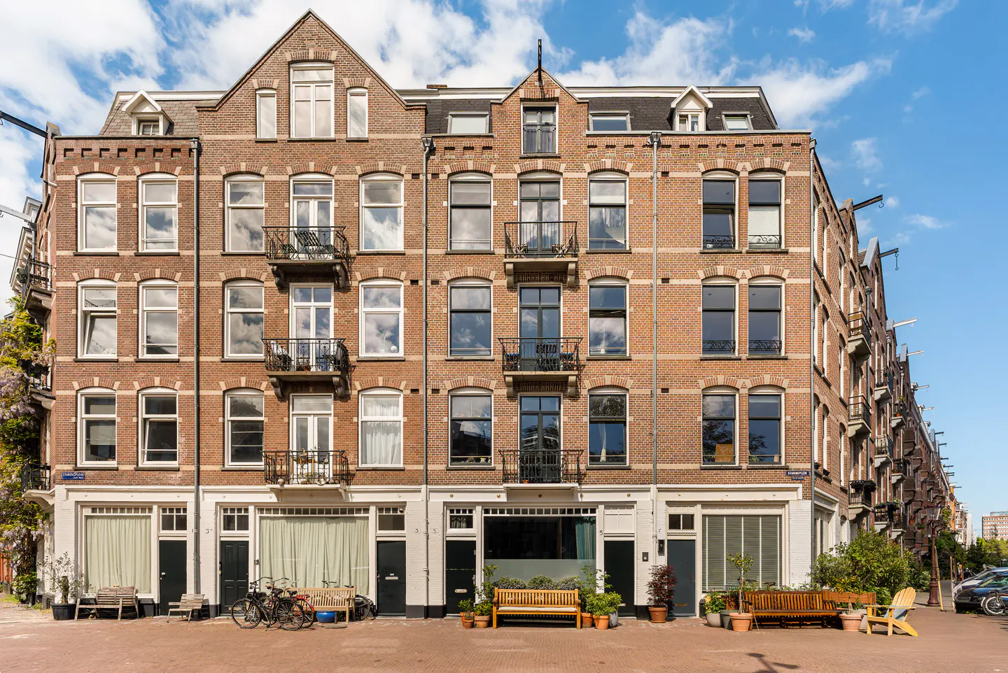 A row of brown brick apartment buildings with black doors and benches in front.