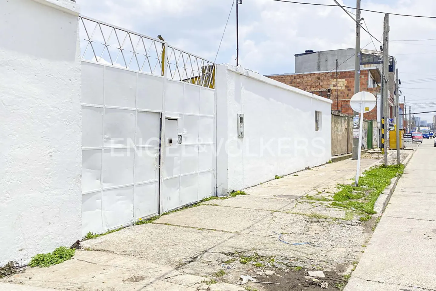 Exterior view of a white gated property with a sidewalk and street. The gate is metal with a diamond pattern on top.