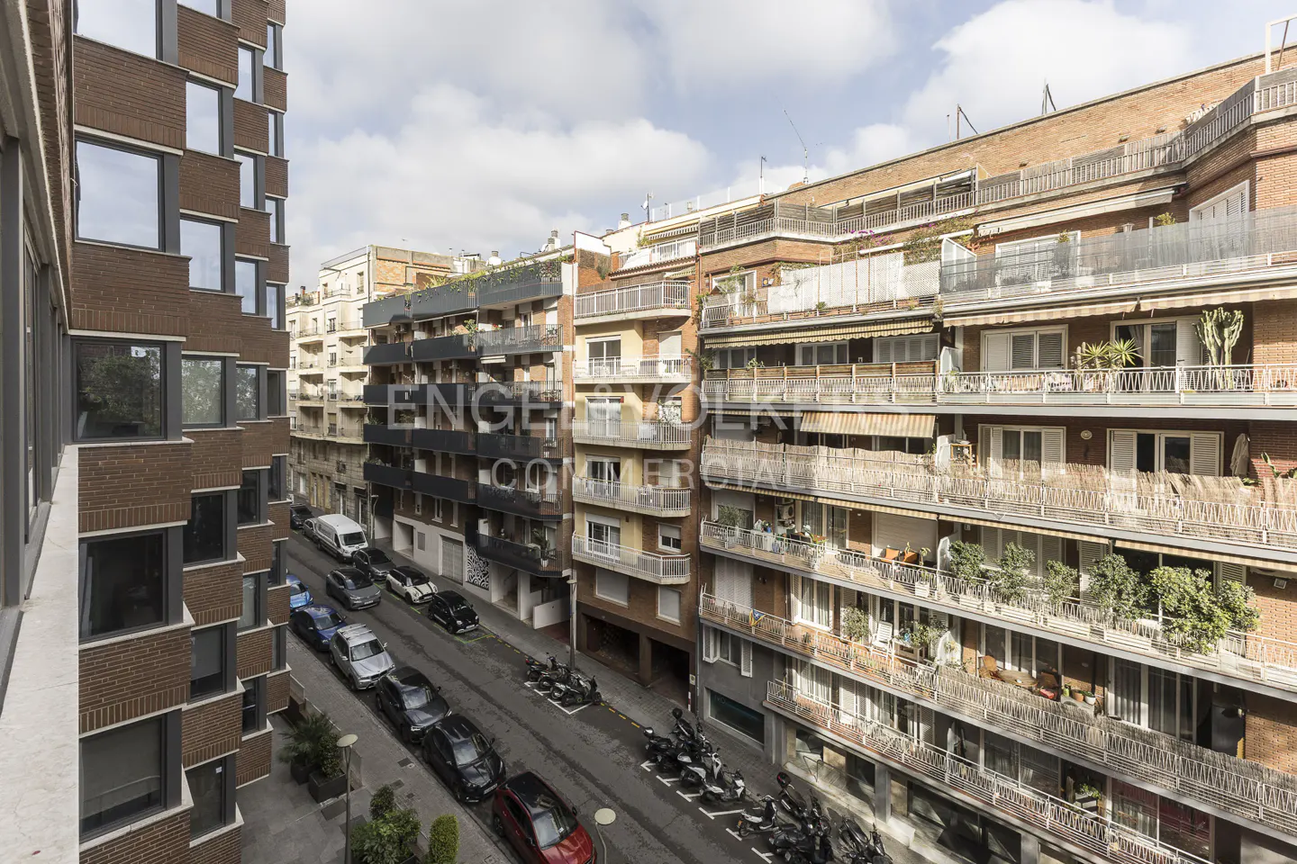 High-angle view of a narrow city street lined with multi-story brick apartment buildings featuring balconies and parked cars.