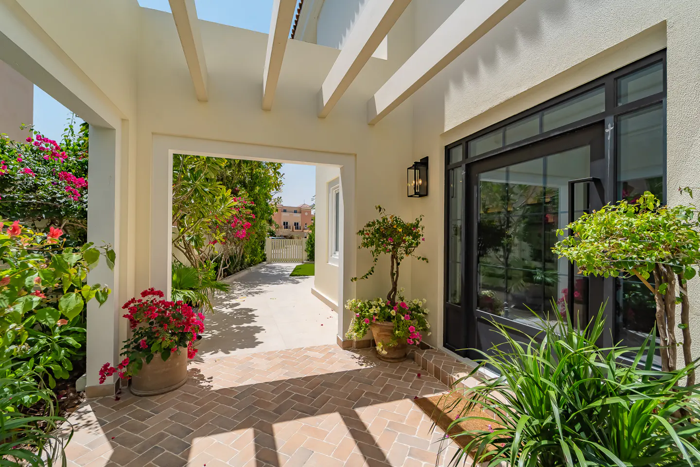 Exterior view of a home's entrance with brick flooring, potted plants, and a black-framed glass door.