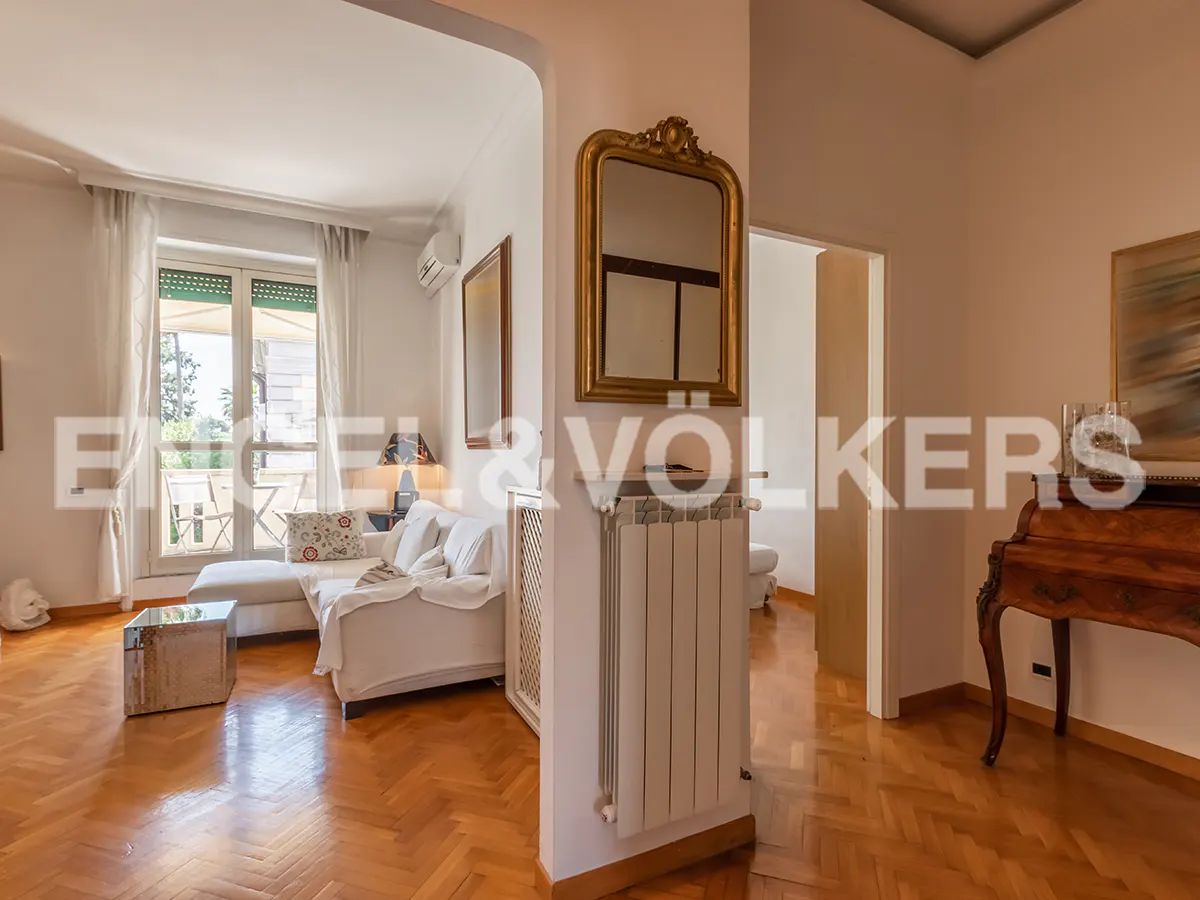 A bright apartment interior with herringbone wood floors, a white sofa, and a gold-framed mirror.