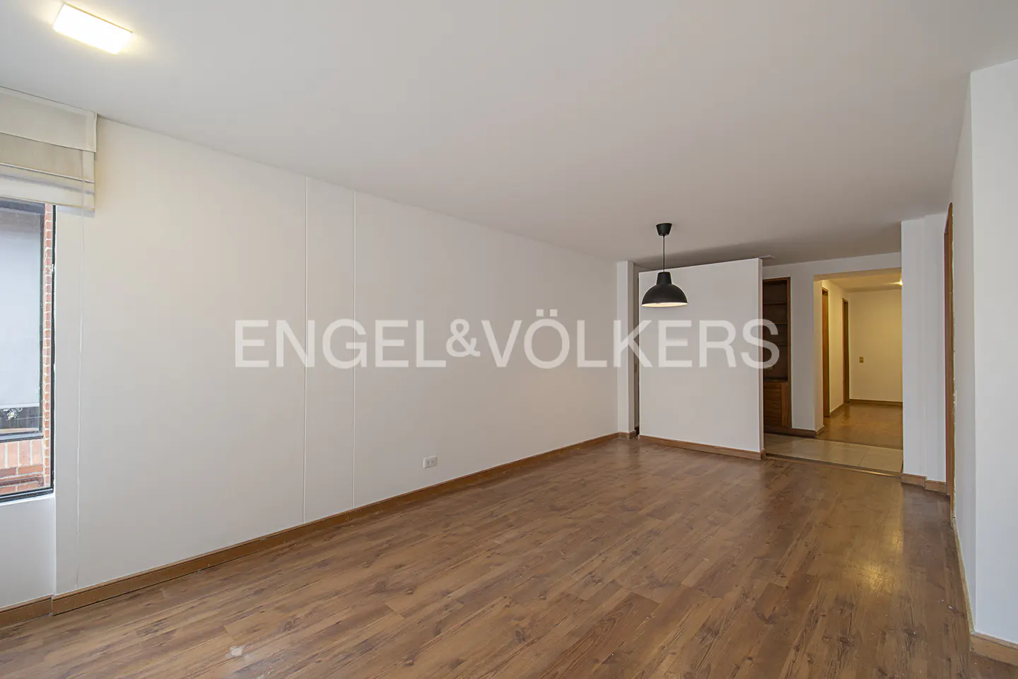 Empty room with wood floors, white walls, and a black pendant light. Engel & Völkers logo on the wall.