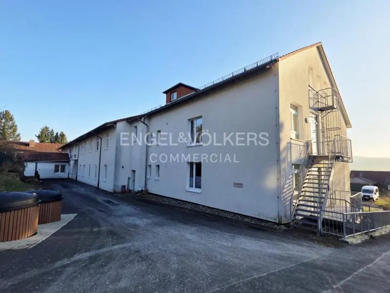 Exterior view of a long, light gray commercial building with a metal staircase on the right side and the Engel & Völkers logo on the facade.