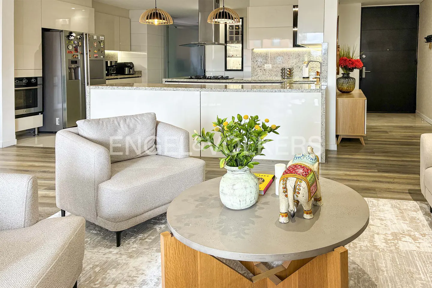 Modern living room with light gray armchairs, a round coffee table with a plant and elephant figurine, and a white kitchen.