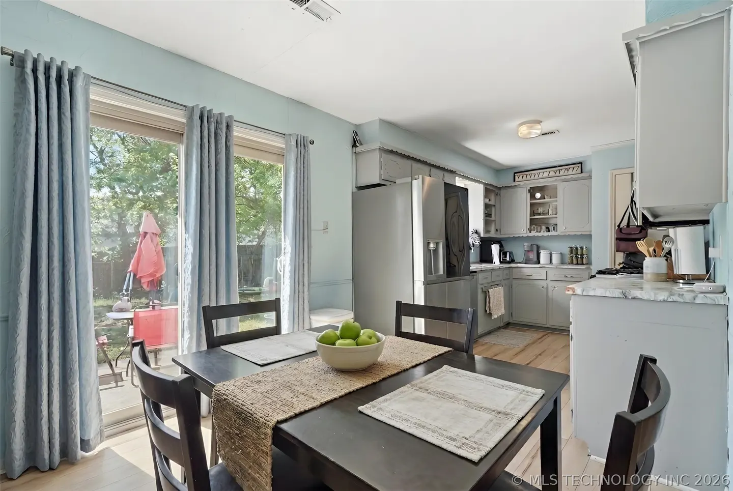 A bright kitchen with a dark wood table set with a bowl of green apples. Sliding glass doors lead to a patio with a red umbrella.