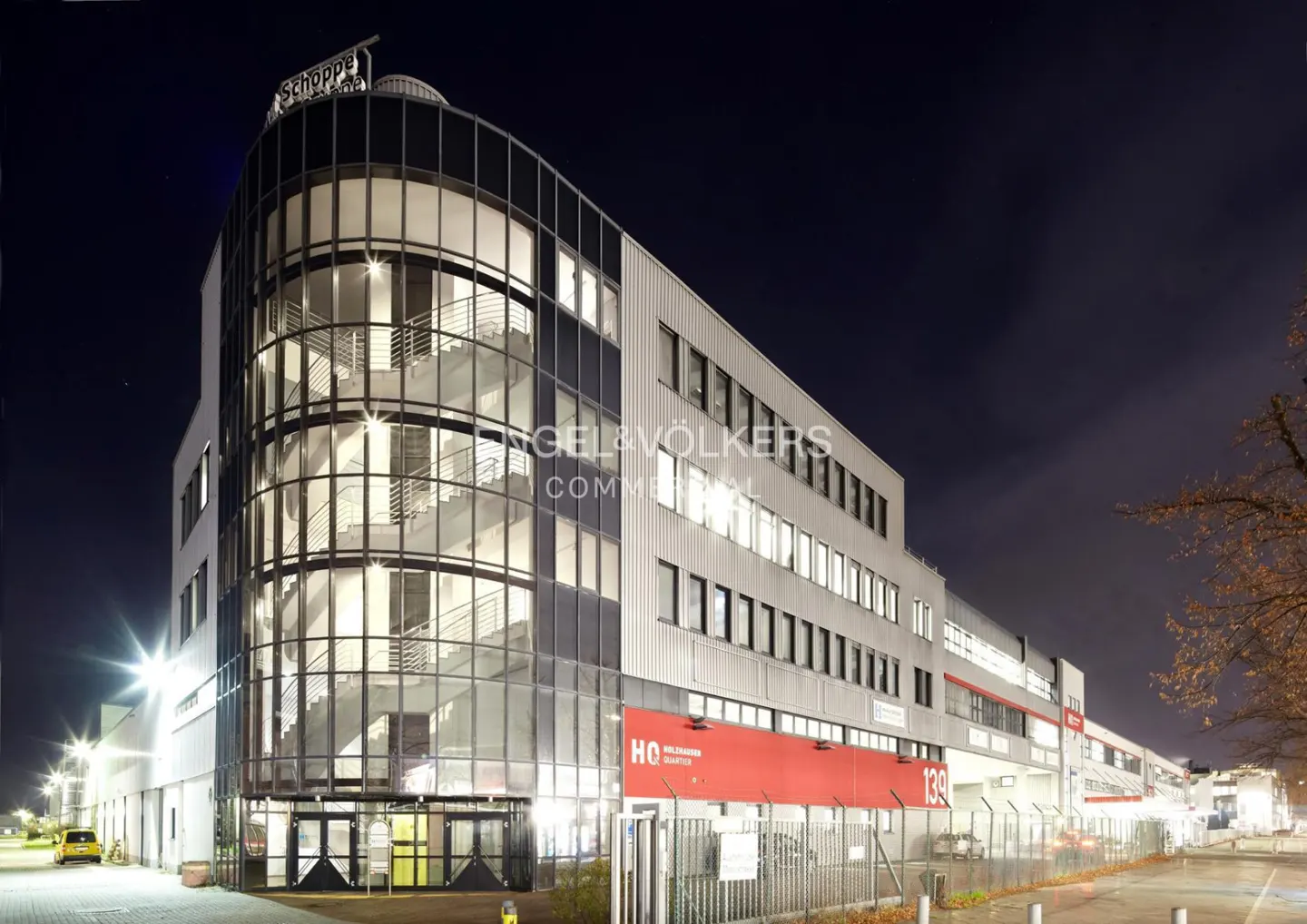 Exterior night shot of a modern commercial building with glass staircase and red signage.