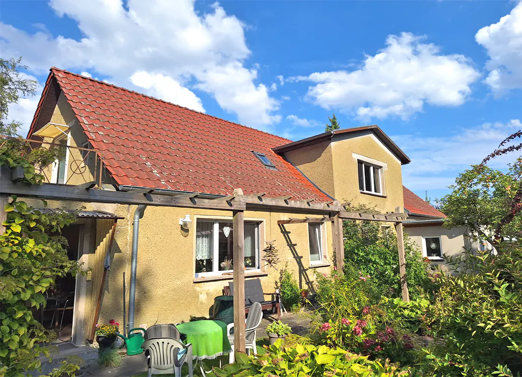 Exterior view of a yellow stucco house with a red tile roof and a garden patio.