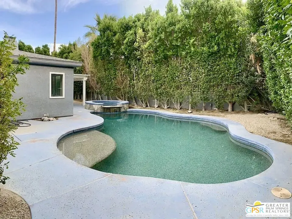 A backyard with a turquoise pool, a gray house, and green trees.