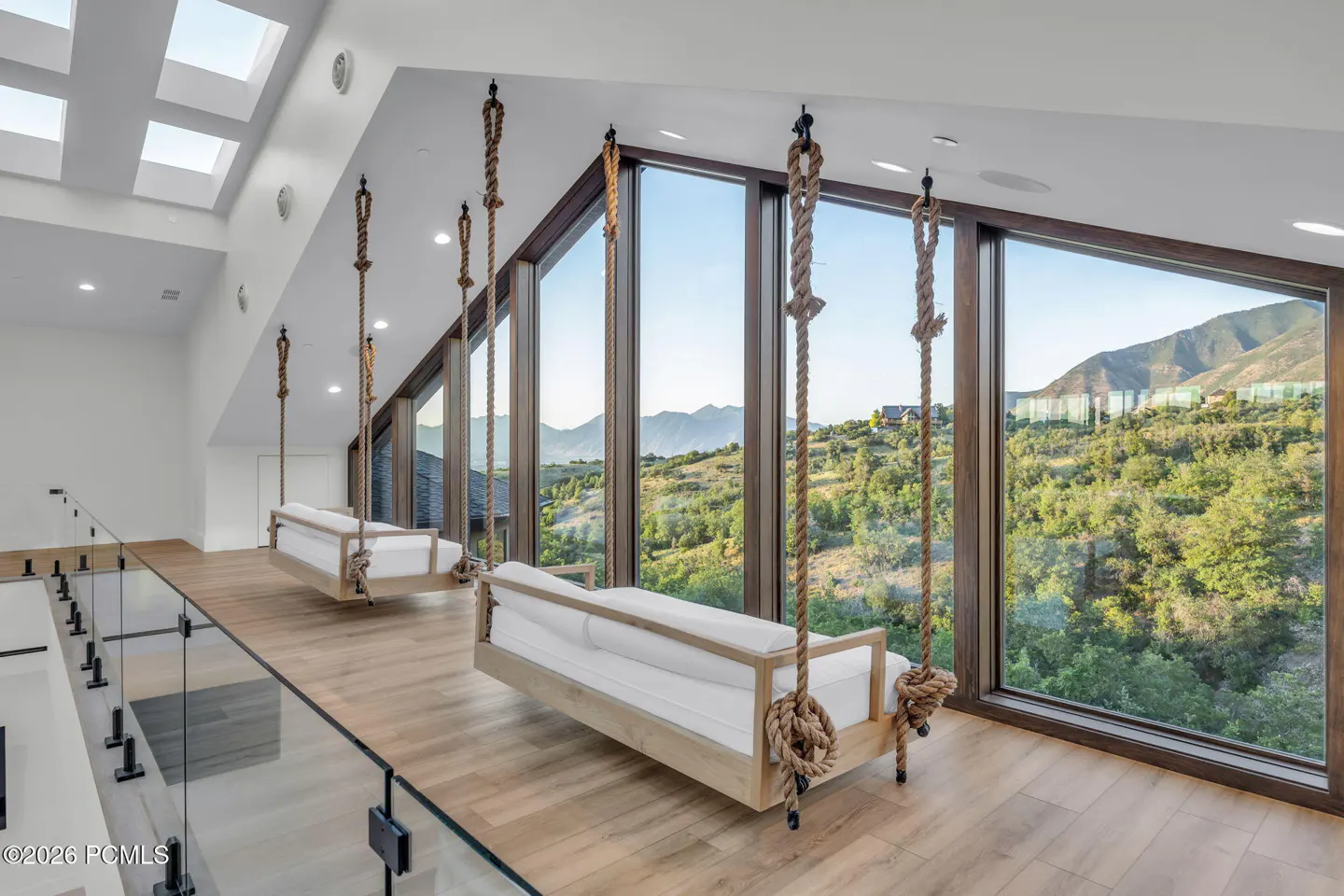 Bright room with two rope swings with white cushions, hanging in front of large windows with mountain views.