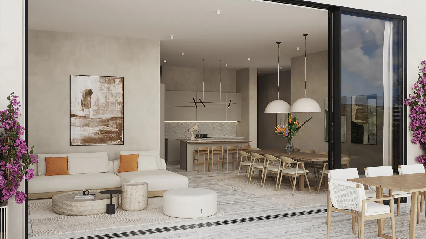 Open-concept living space with a white sofa, dining table, and kitchen. Large sliding glass doors lead to an outdoor patio with purple flowers.