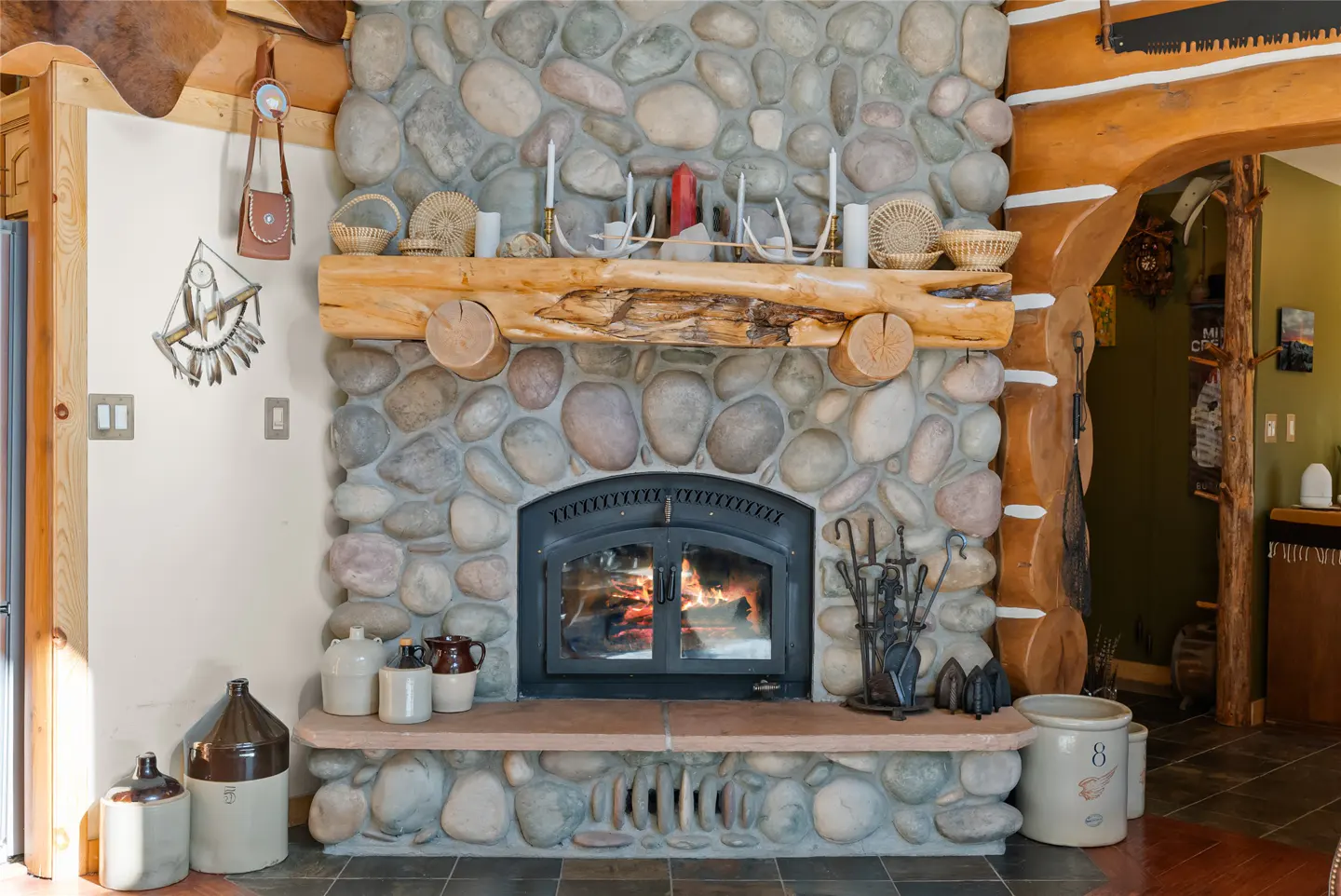 Stone fireplace with a wood mantel, decorated with baskets, candles, and antlers. Fire is burning in the black metal fireplace insert.