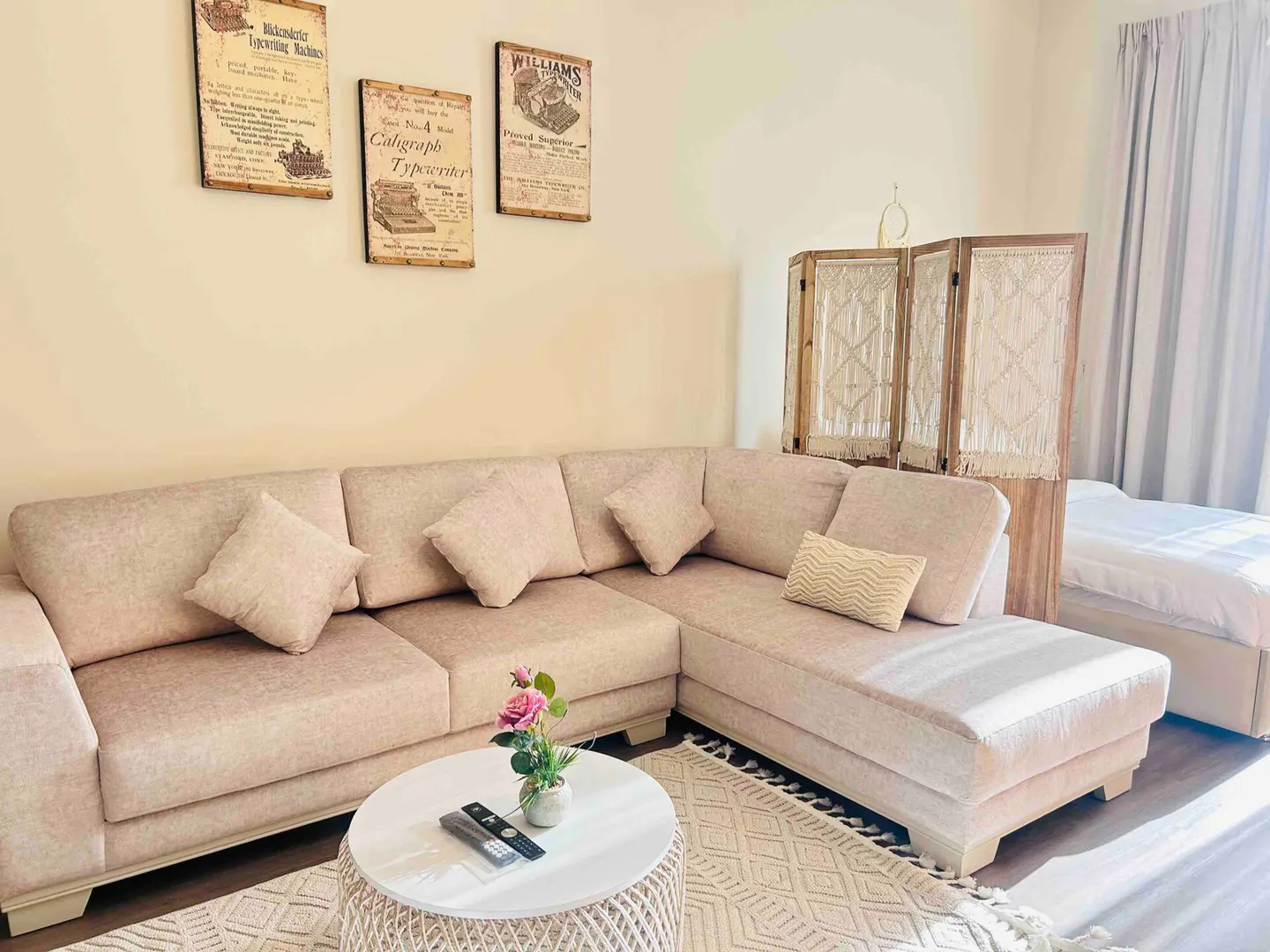 Living room with a beige sectional sofa, pillows, round table with flowers, and vintage typewriter art on the wall.