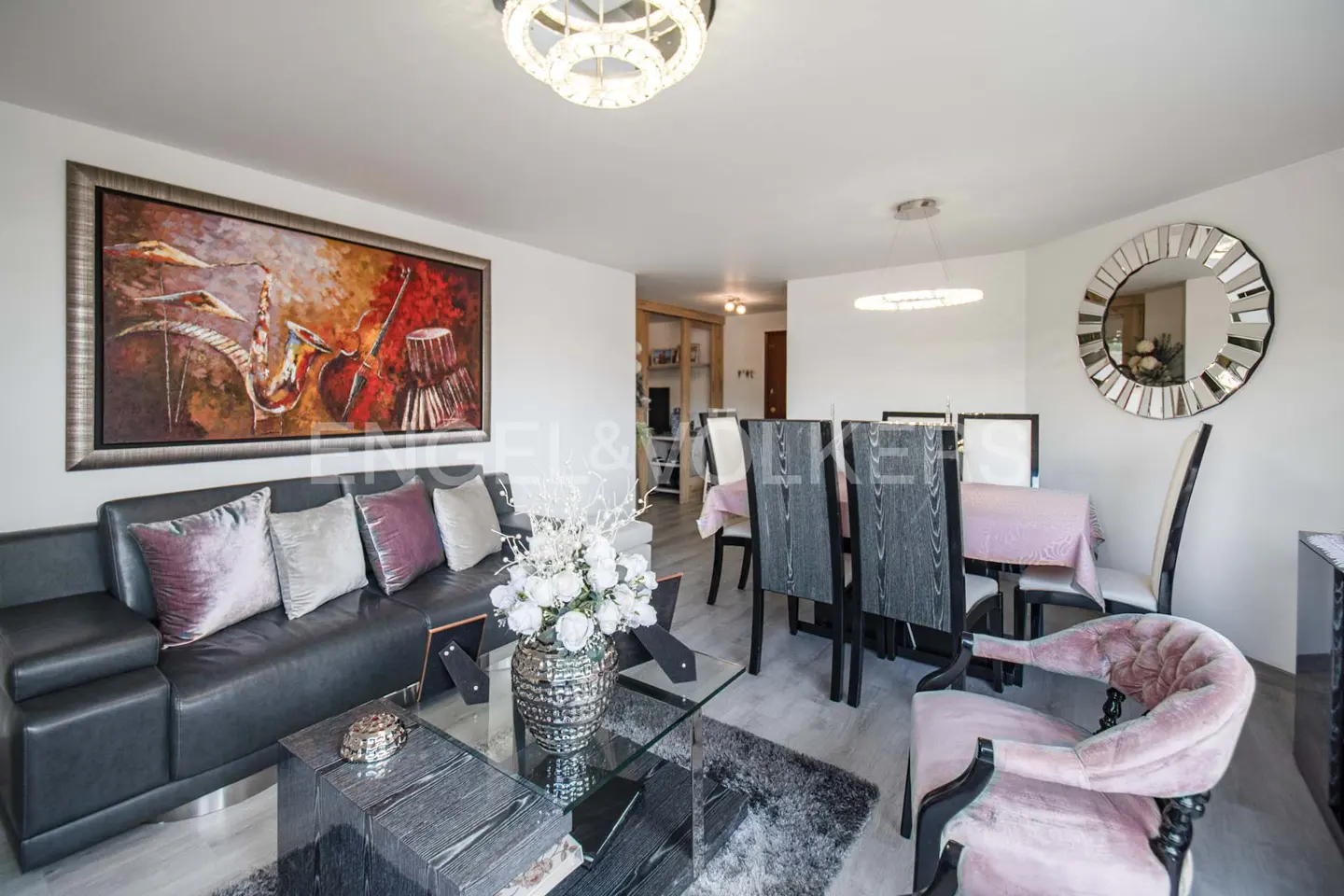 Living room with a black leather sofa, a glass coffee table, and a dining table with chairs. A large painting hangs on the wall.