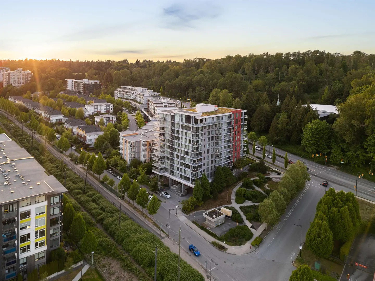 Aerial view of a modern, multi-story apartment building with red accents, surrounded by trees, roads, and other residential buildings.