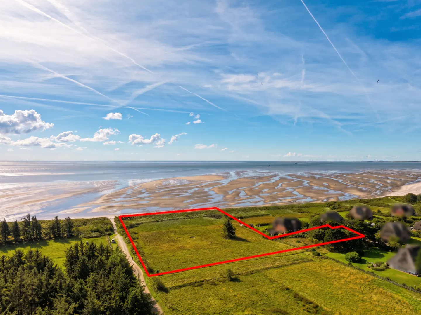 Aerial view of a grassy plot outlined in red, near a beach under a blue sky.