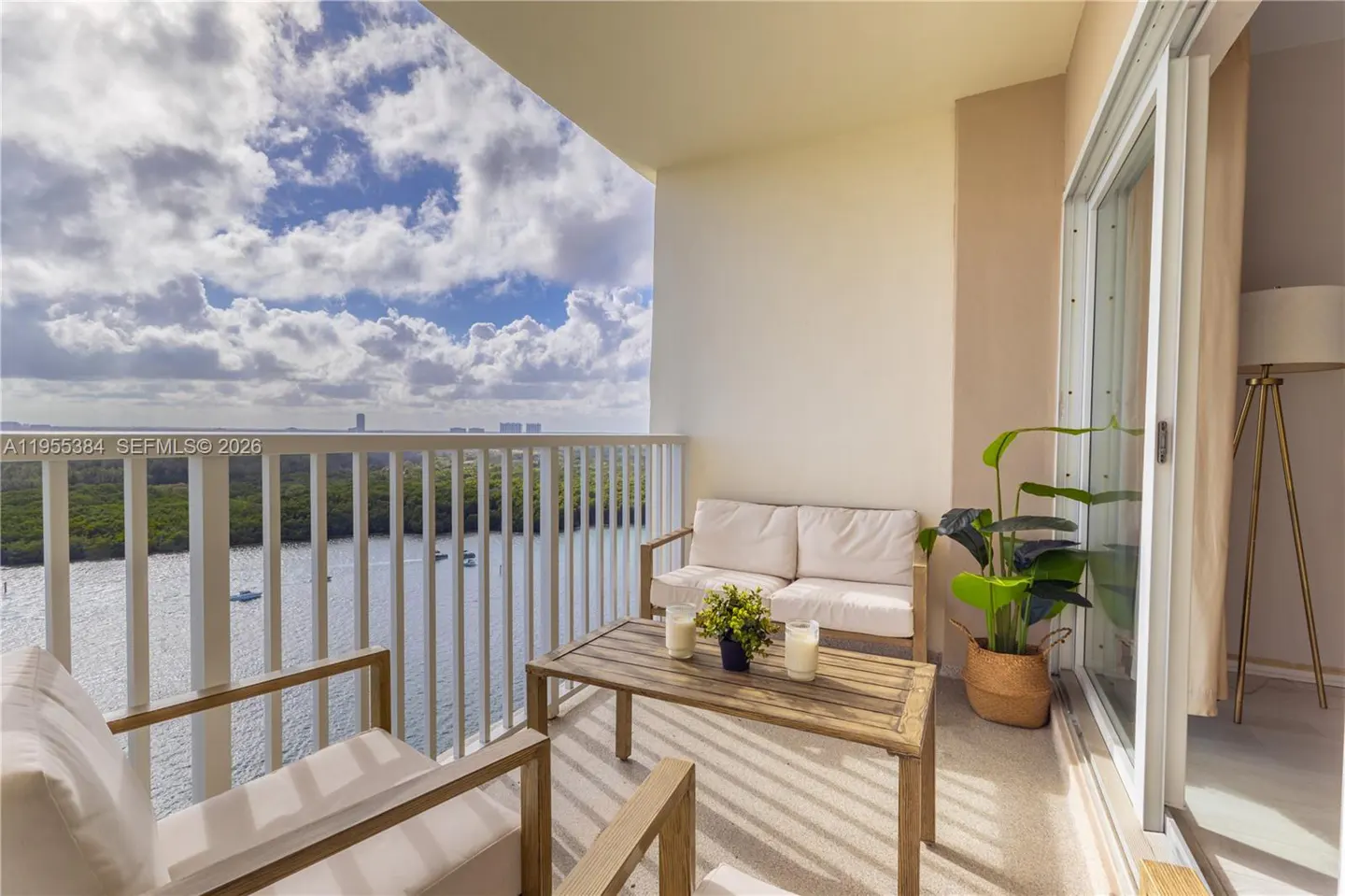 Balcony with white furniture, a wood table, and a view of a river and trees under a cloudy sky.