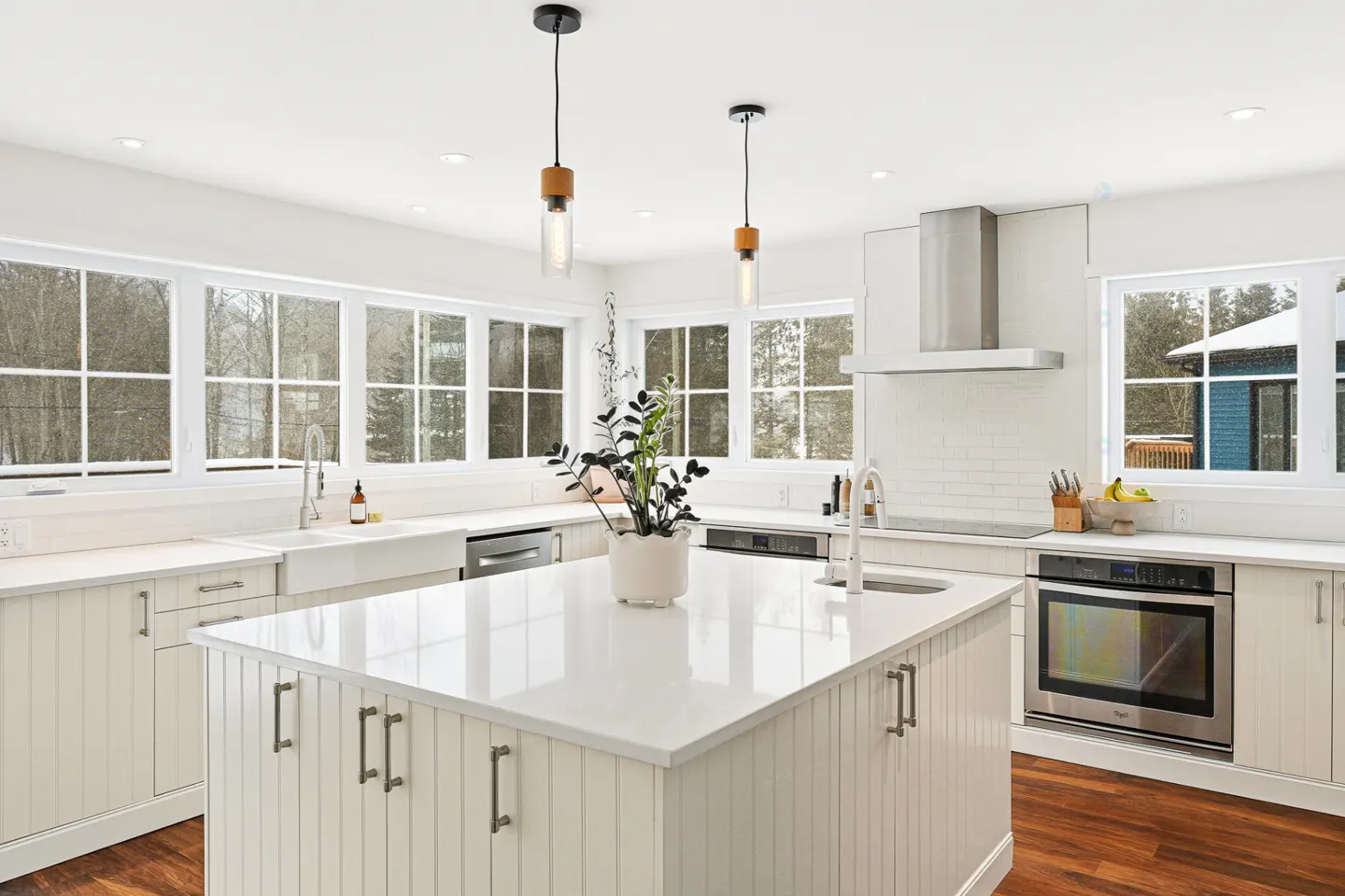 Bright, modern kitchen with white cabinets, a large island, and wood floors. Large windows offer a view of a snowy landscape.