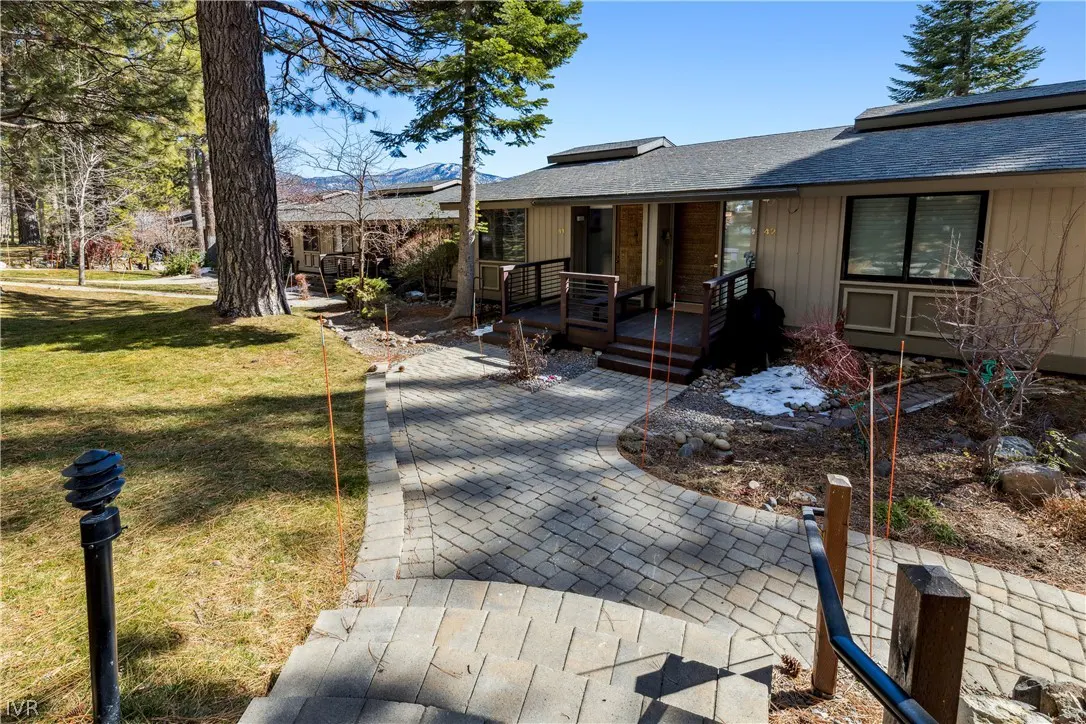 Exterior view of a tan condo with a gray roof, a brick walkway, and green grass.