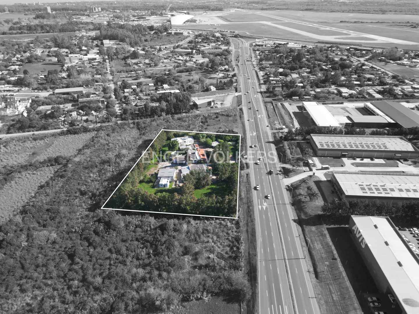 Aerial view of a property outlined in white, next to a highway and airport runway in a black and white landscape.
