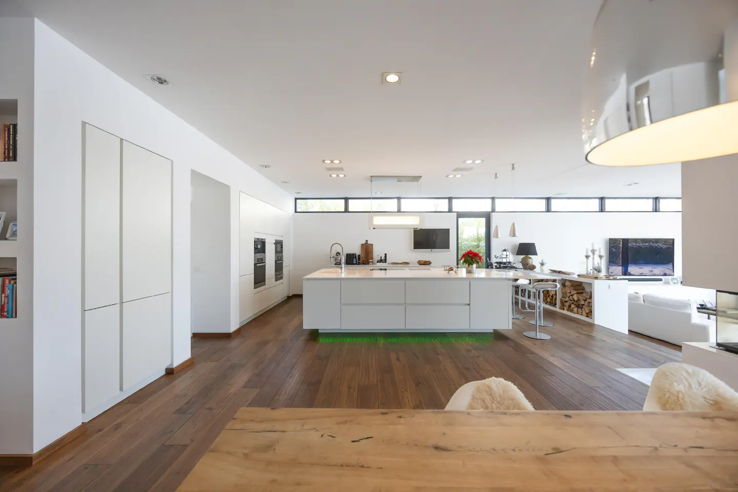 Open-concept kitchen and living room with white walls, wood floors, and a large island. Modern design with natural light.