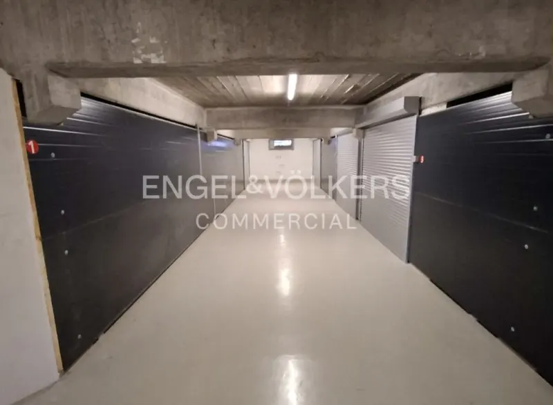 Interior view of a storage unit hallway with black and silver units, a concrete ceiling, and a light gray floor.