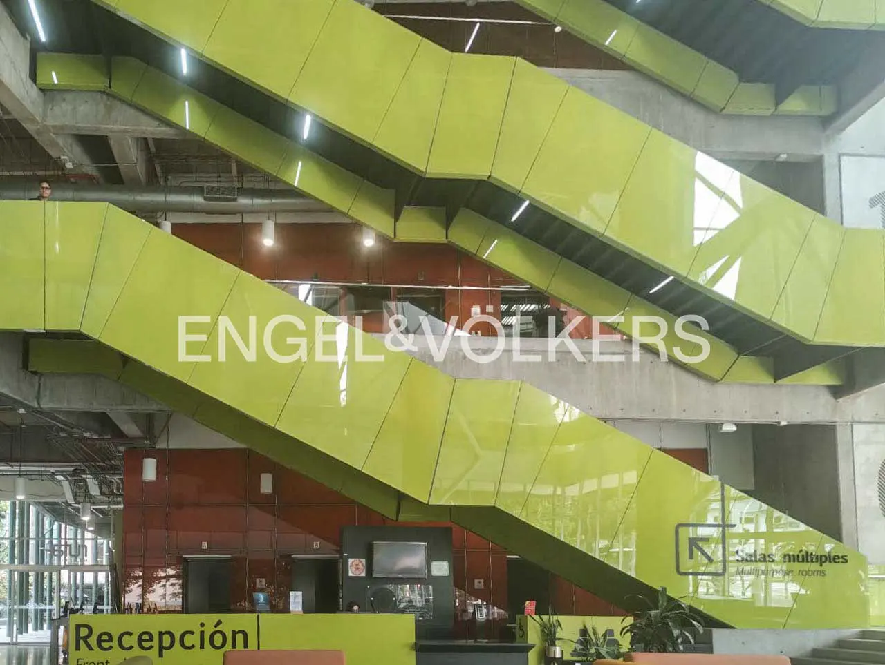 Interior view of a modern building with lime green stairs, a reception desk, and the Engel & Völkers logo.