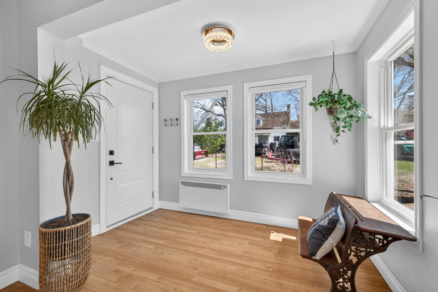 Bright entryway with light wood floors, white walls, a potted plant, a vintage wooden bench, and two windows.