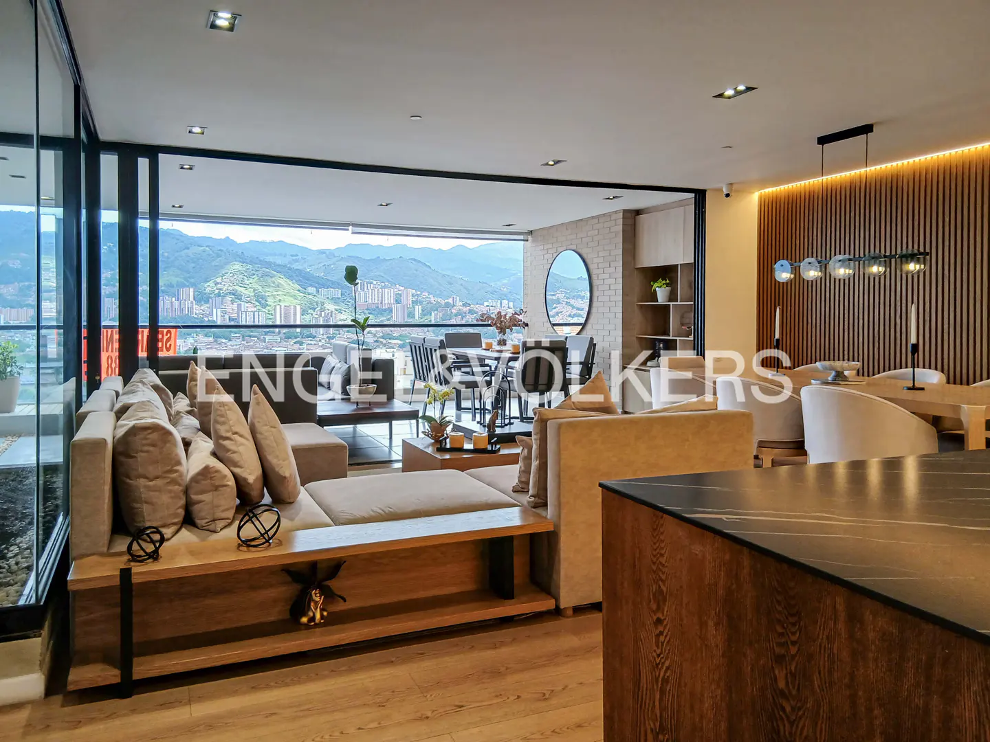 A modern living room with a beige sofa, wood floors, and a city view. A dining table and chairs are visible in the background.