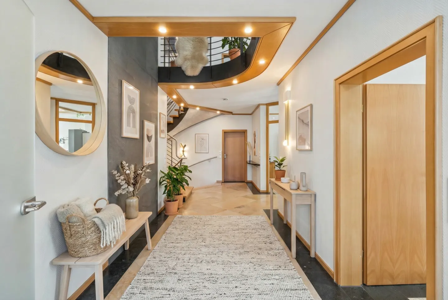Bright hallway with a round mirror, bench with basket, and a long rug leading to a curved staircase.