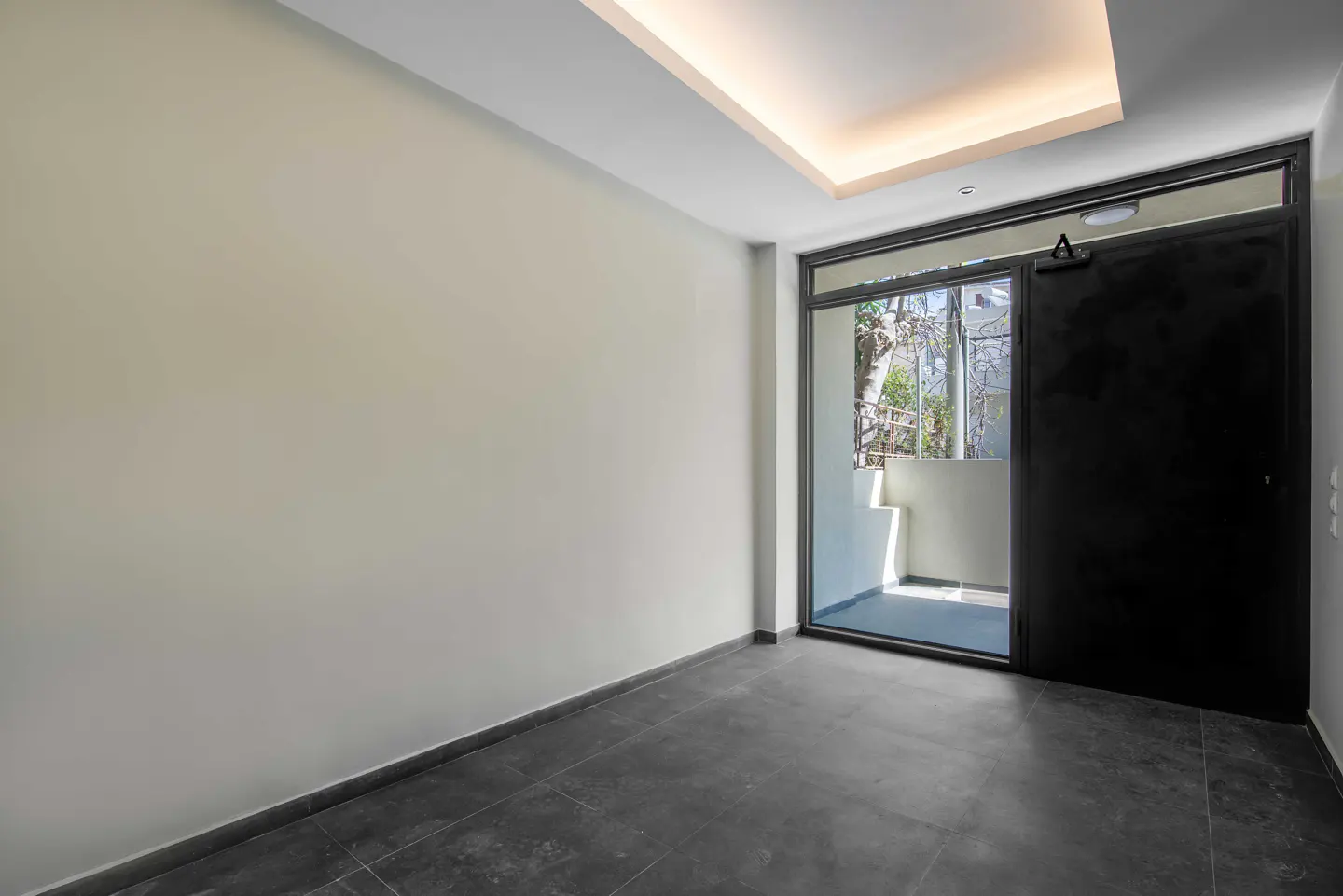 Empty room with gray tile floor, cream walls, and a black sliding glass door to a balcony. A recessed light is in the ceiling.