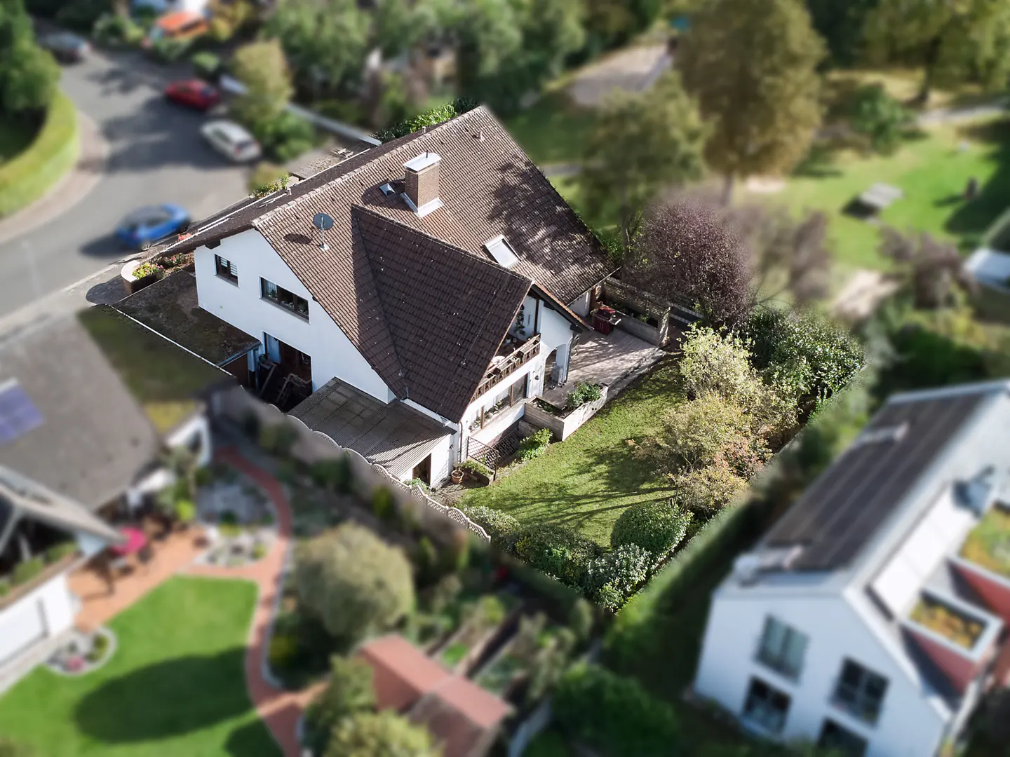 Aerial view of a white house with a brown roof, chimney, and satellite dish, surrounded by green trees and lawns.
