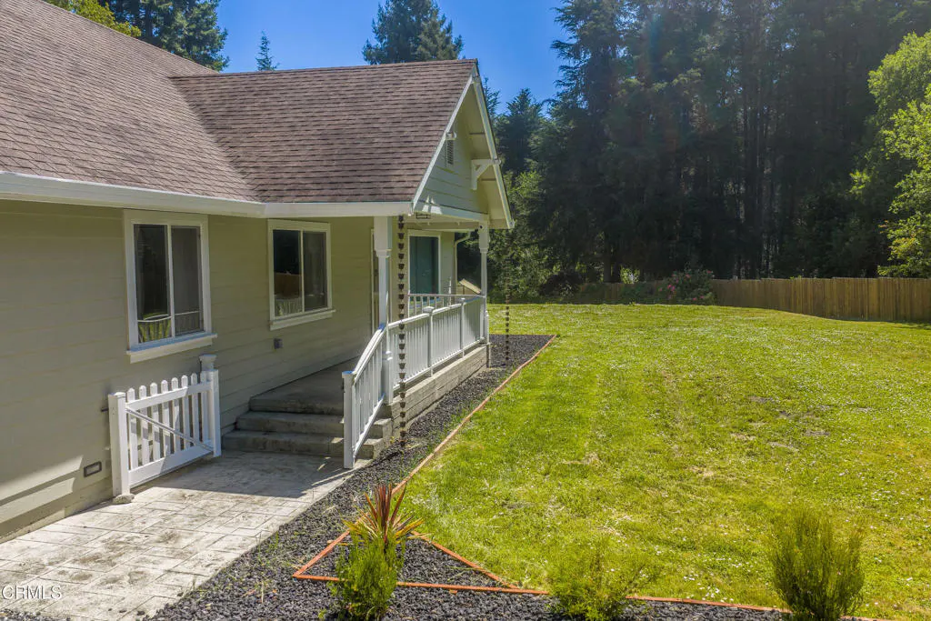 Exterior view of a light green house with a brown roof, white trim, and a large green lawn. A white picket fence and porch with white railings are visible.