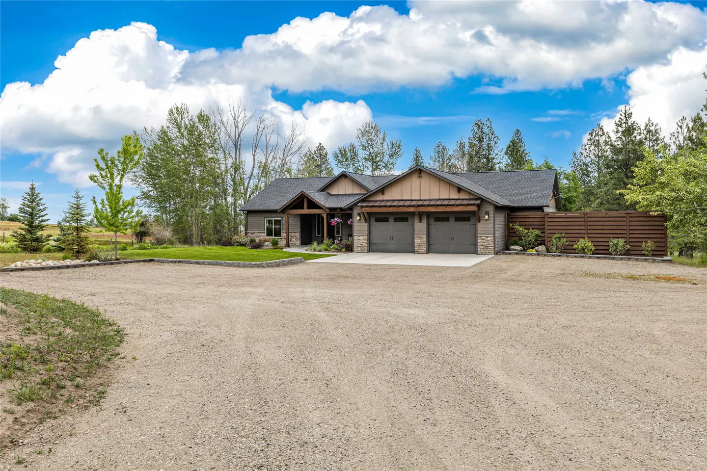 A single-story home with a gray roof, two-car garage, and gravel driveway on a sunny day.