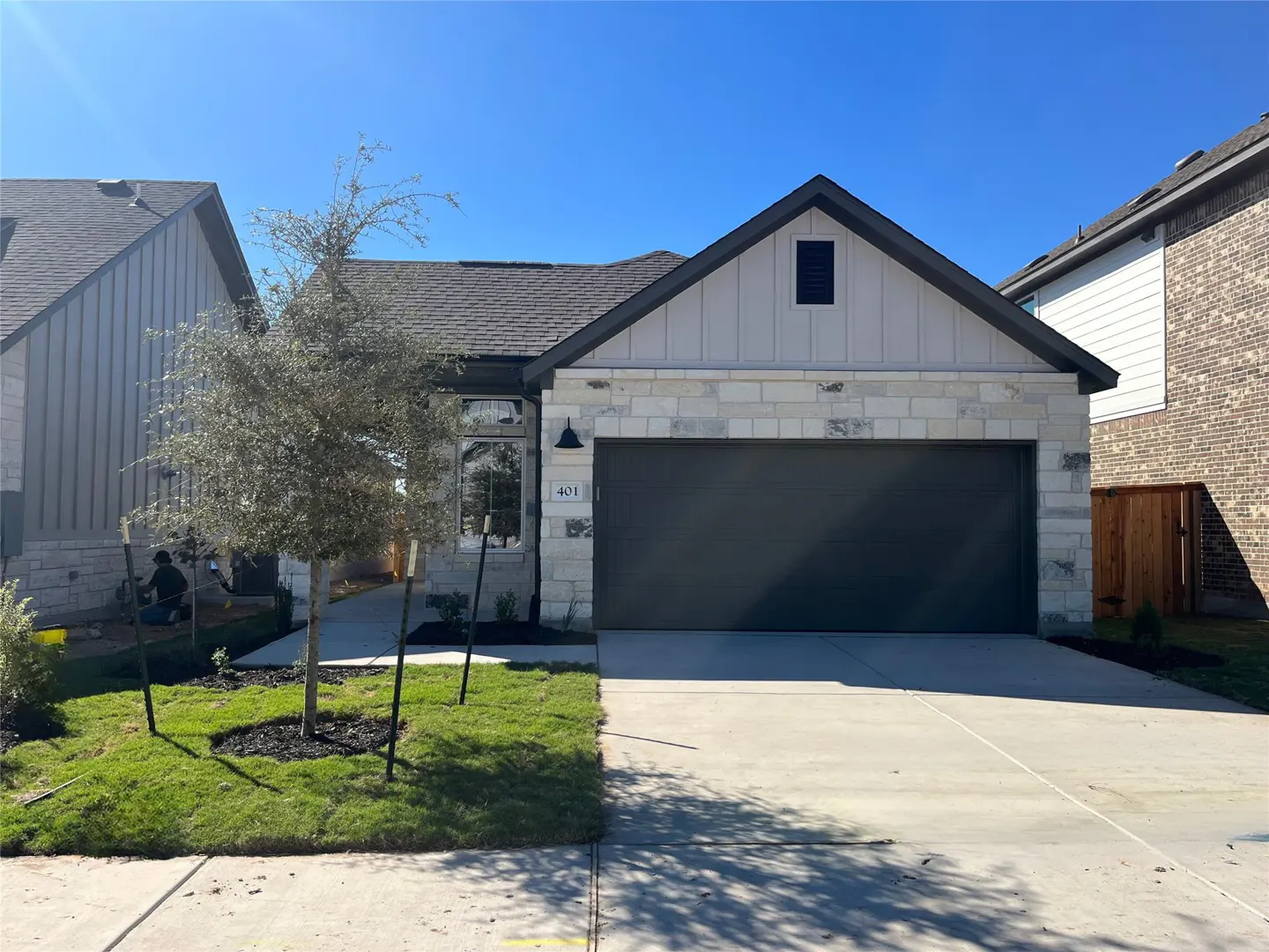 A single-story house with a gray roof, stone and white siding, a dark gray garage door, and a green lawn.