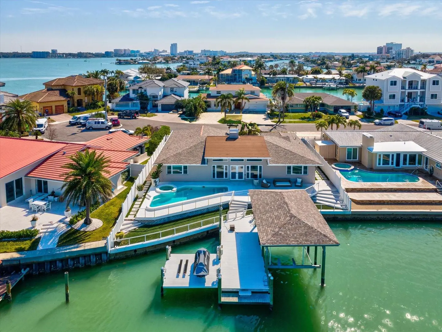 Aerial view of a waterfront home with a pool, dock, and boat lift on a sunny day.