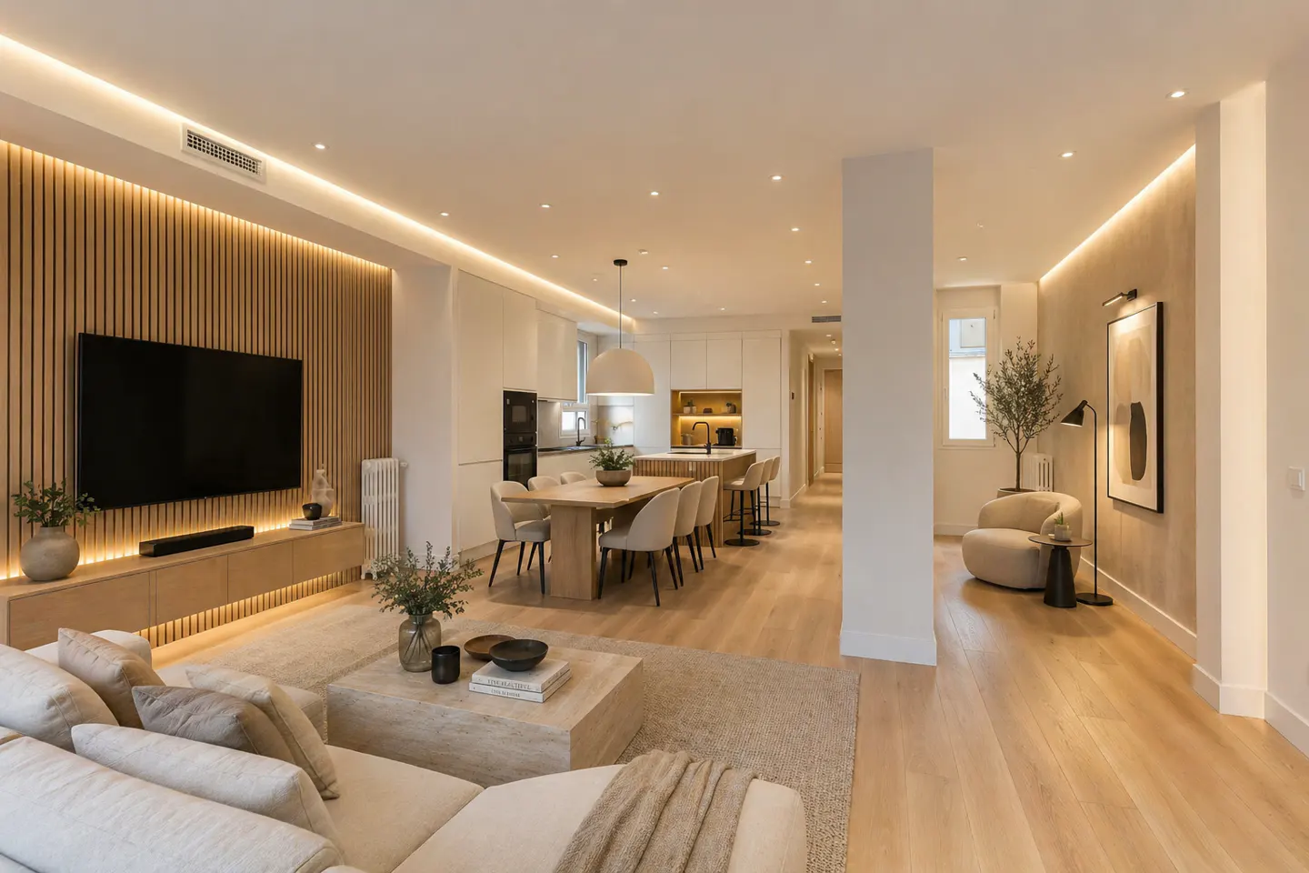 Open-concept living space with a sofa, TV, dining table, and kitchen. The color palette is neutral with wood accents and warm lighting.