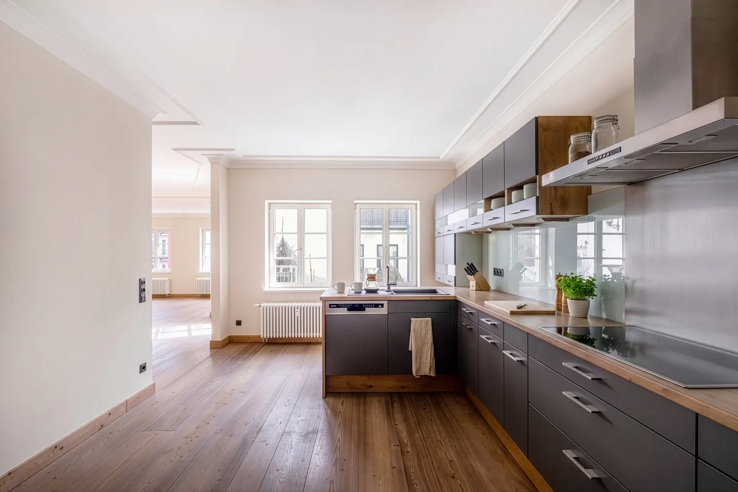 A bright kitchen with gray cabinets, wood countertops, and hardwood floors. Two windows let in natural light.