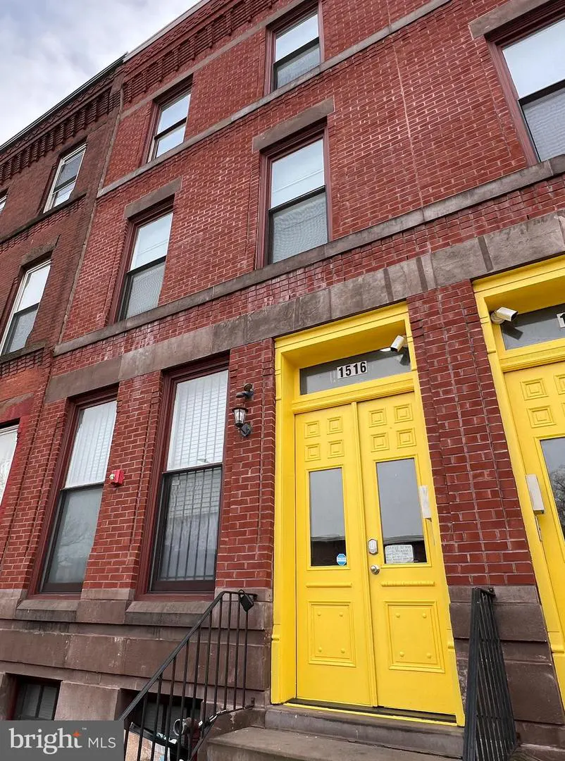 Exterior of a red brick row house with bright yellow double doors and the number 1516 above.
