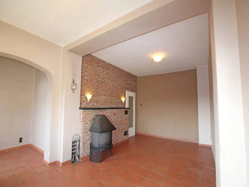 Living room with brick accent wall, wood-burning stove, and terracotta tile floor. Walls are beige.