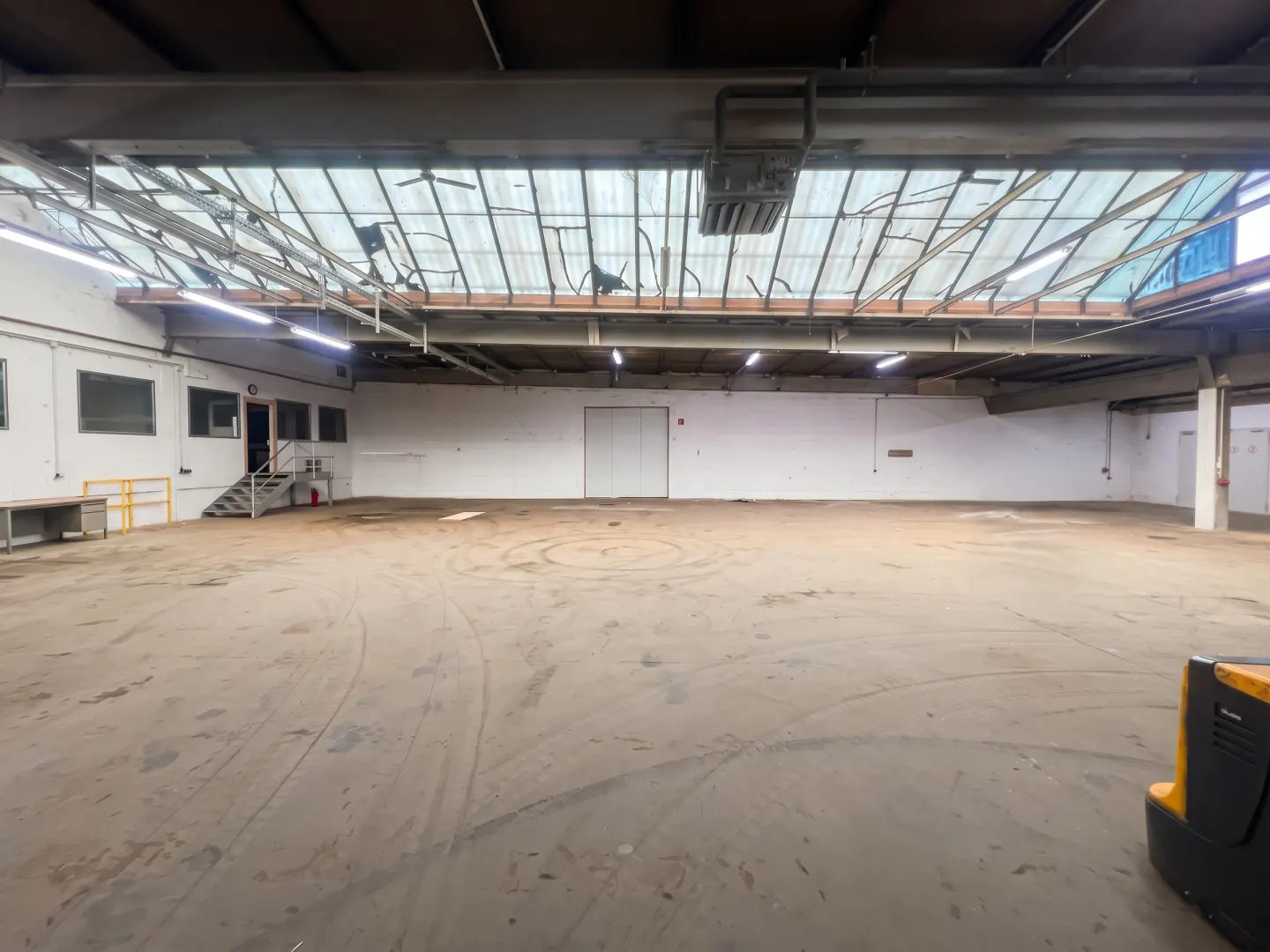 A large, empty warehouse with white walls, a concrete floor, and a skylight.