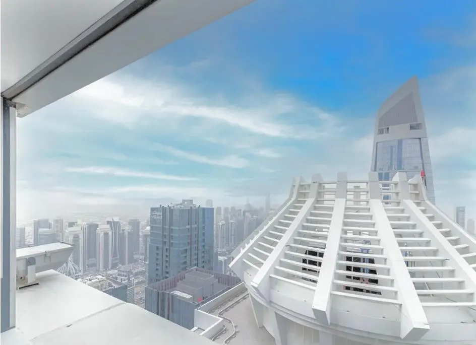 View from a high-rise balcony shows a city skyline with modern buildings under a blue sky with light clouds.