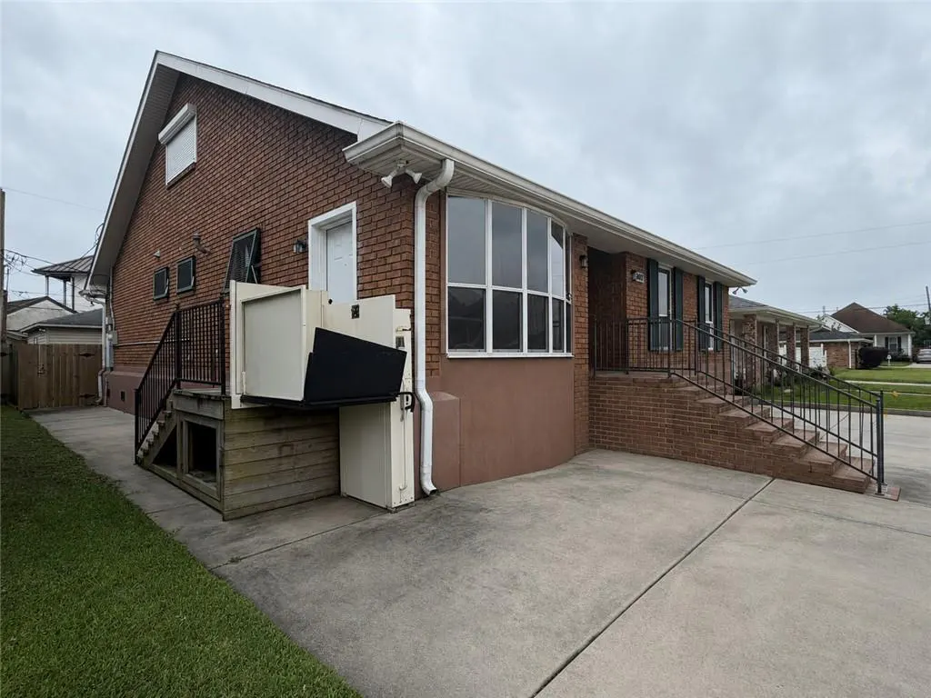 Exterior view of a brick house with a wheelchair lift, stairs, and a concrete driveway. The sky is overcast.