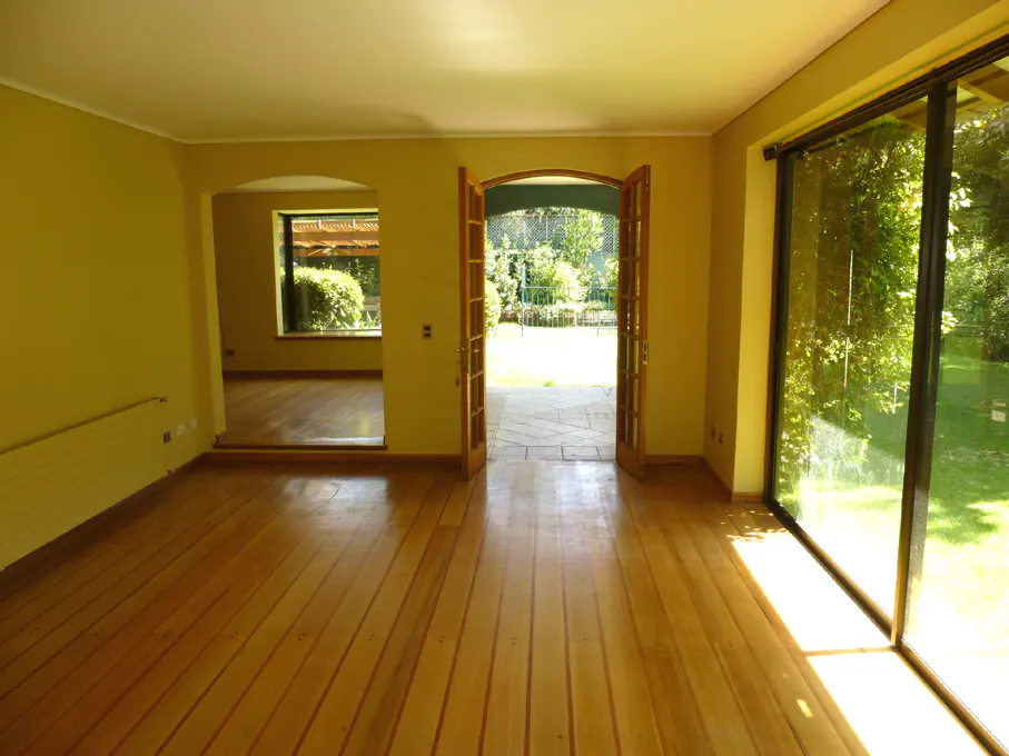 Empty room with wood floors, yellow walls, and open double doors leading to a garden. Large glass sliding doors on the right.