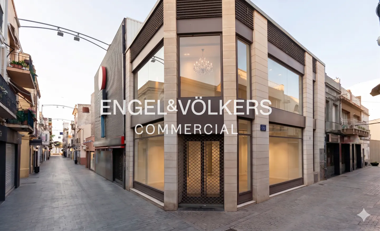 Engel & Völkers Commercial building on a cobblestone street. The building has large windows and a chandelier is visible inside.